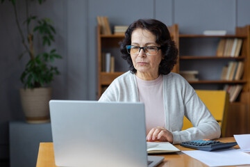 Middle aged senior woman sit with laptop and paper document, Pensive older mature lady reading paper bill pay online at home managing bank finances calculating taxes planning loan debt pension payment - obrazy, fototapety, plakaty