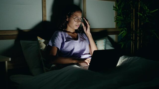 Young african american woman using laptop tired sitting on bed at bedroom