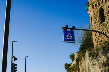 A pedestrian crossing road sign on the background of a blue sky and a medieval castle next to the...