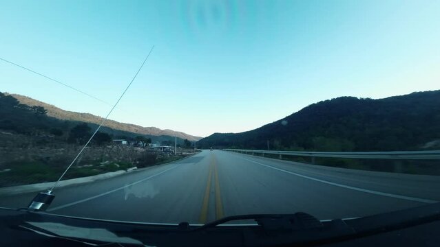 Viajando entre Monta&ntilde;as y carretera, rebasando autos en un atardecer que pega en la monta&ntilde;a de fondo los rayos del sol. 