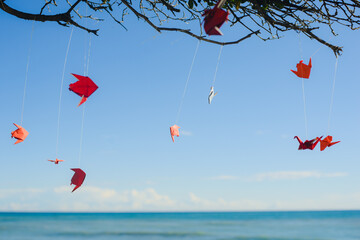 Red origami figures on a tree branch by the sea