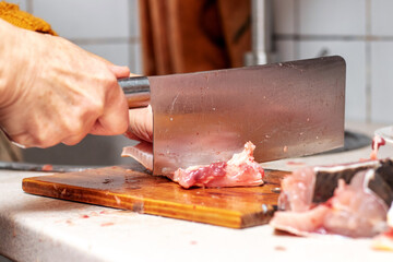 A woman cuts fish with a large knife at home in the kitchen