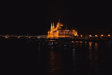 Obraz premium The Hungarian Parliament in Budapest near the Danube River is illuminated by street lights.