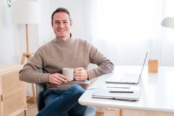 Cheerful man with coffee and laptop at home