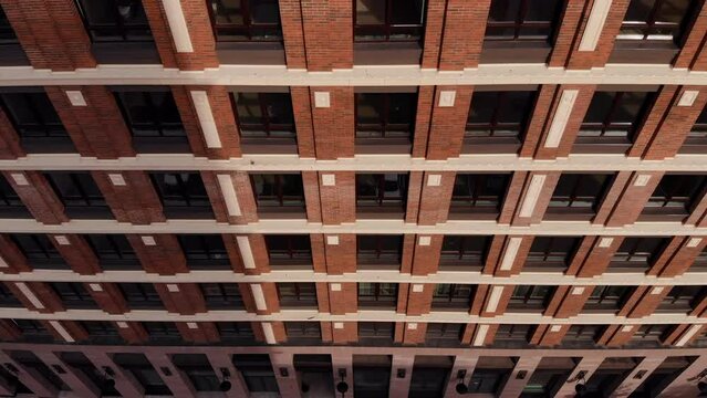 Exterior view of a high-rise multistory building. Aerial view of the facade of a brick building with windows. Dark window frames. Drone view. Brick wall. Takeoff up parallel to the building