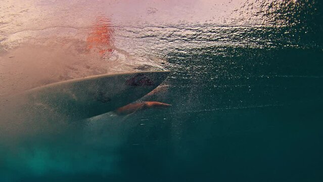 Surfer underwater. Man dives under the wave with surfboard to pass the wave, speed warped version of the footage. Underwater view of the surfer duck diving under the wave