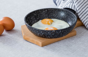 Fried eggs in a frying pan and chicken eggs on a linen tablecloth. Breakfast, lunch and dinner. The view is soft, selective focus. Rustic style.