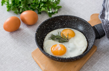 Fried eggs in a frying pan with rosemary, bread, eggs and green salad on a linen tablecloth. Breakfast, lunch and dinner. The view is soft, selective focus. Rustic style.