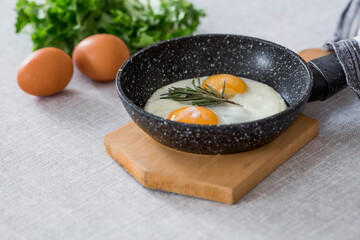 Fried eggs in a frying pan with rosemary, bread, eggs and green salad on a linen tablecloth. Breakfast, lunch and dinner. The view is soft, selective focus. Rustic style.
