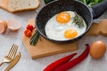 Fried eggs in a frying pan with rosemary, bread, eggs and green salad on a linen tablecloth. Breakfast, lunch and dinner. The view is soft, selective focus. Rustic style.