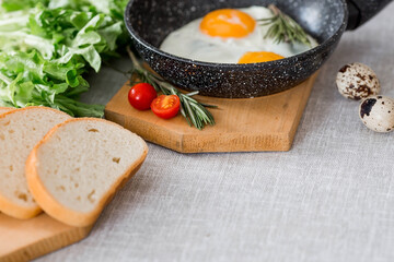 Fried eggs in a frying pan with rosemary, bread, eggs and green salad on a linen tablecloth. Breakfast, lunch and dinner. The view is soft, selective focus. Rustic style.