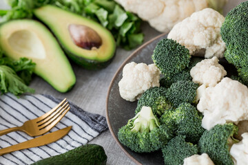 Fresh green broccoli, cauliflower and avocado on a plate on a linen tablecloth. Broccoli cabbage leaves. Light background. Vegetarian food. Healthy lifestyle.