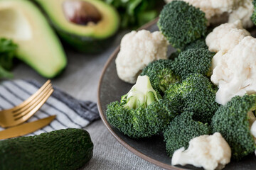 Fresh green broccoli, cauliflower and avocado on a plate on a linen tablecloth. Broccoli cabbage leaves. Light background. Vegetarian food. Healthy lifestyle.