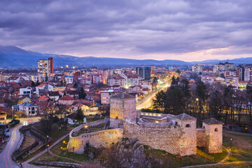 Purple sky above Pirot cityscape with foreground ancient fortress and city lights at winter - 568190785