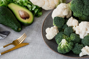 Fresh green broccoli, cauliflower and avocado on a plate on a linen tablecloth. Broccoli cabbage leaves. Light background. Vegetarian food. Healthy lifestyle.