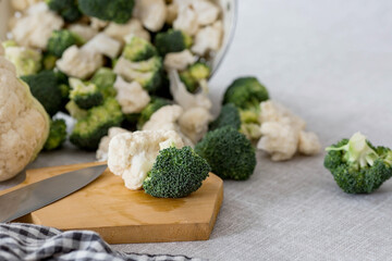 Fresh green broccoli and cauliflower on a wooden chopping board on a linen tablecloth. Broccoli cabbage leaves. Light background. Vegetarian food. Healthy lifestyle.