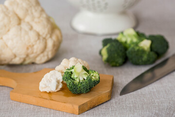 Fresh green broccoli and cauliflower on a wooden chopping board on a linen tablecloth. Broccoli cabbage leaves. Light background. Vegetarian food. Healthy lifestyle.