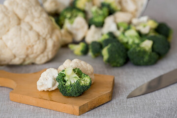 Fresh green broccoli and cauliflower on a wooden chopping board on a linen tablecloth. Broccoli cabbage leaves. Light background. Vegetarian food. Healthy lifestyle.
