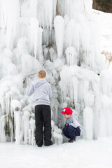 Young boys play together outdoor, next to a frozen waterfall at winter time.