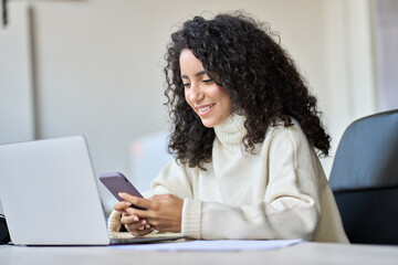Young happy business woman, smiling professional businesswoman looking at smartphone using cellphone mobile cell tech working in office typing on cell phone searching job online sitting at desk.