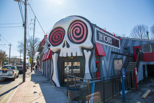 The Vortex Bar and Grill with a skull over the top of the door,, bare winter trees, cars and trucks driving on the street and a clear blue sky in Little Five Points in Atlanta Georgia USA