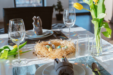 Beautiful Easter table setting with festive decor indoors. Napkin in shape of rabbit ears, colorful...