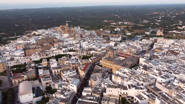 Aerial panoramic drone footage of Ostuni - La Citta Bianca (white city), Puglia, Italy at sunset. View of Cathedral, main square, the medieval historic old town landmark tourist destination from above