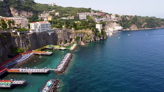 Aerial drone footage of Bagni Salvatore at steep cliff coastline of Sorrento town, Campania, Italy. Summer beach resort platforms on Sorrentine peninsula with people sunbathing on lounger from above.