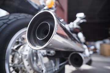 Exhaust chrome pipe of an old touring motorcycle in close-up, against the background of blurry details