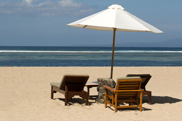 White Parasol with chairs and palm tree leaves on the tropical beach of Sanur on Bali