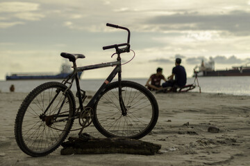 Bike on the beach of Santa Marta, Colombia, with people and boats in the background.