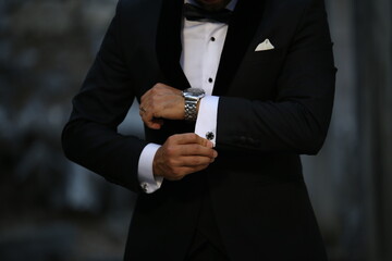 Close-up shot of hands of young white Caucasian male in black tie, fixing his sleeve, sign of...