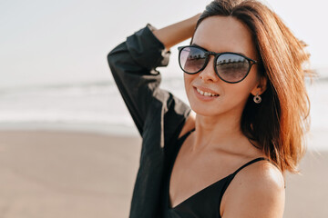 Close up portrait of smiling excited stylish woman with short dark hairstyle posing to camera with happy emotions on blur background of ocean 