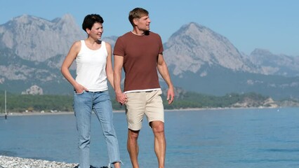 Beautiful middle aged man and woman holding hands while walking on pebble beach