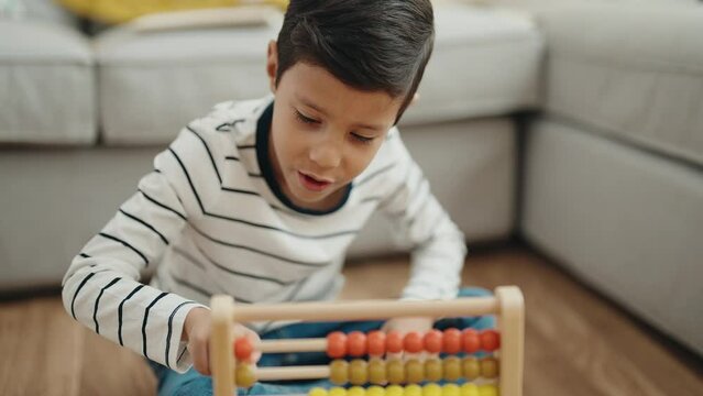 Adorable hispanic boy playing with abacus sitting on floor at home