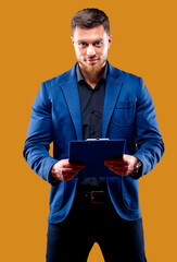 Half-length portrait of handsome young smiling man wearing dark shirt and blue suit holding blue folder, looking at camera. Black background. Money and business concept.