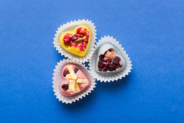 chocolate sweets in the form of a heart with fruits and nuts on a colored background. top view with space for text, holiday concept