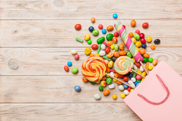 shopping paper gift bag in corner full of assorted traditional candies falling out on colored background with copy space. Happy Holidays sale concept