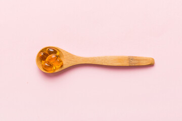 Vitamin omega capsules in a spoon on a colored background. Pills served as a healthy meal. Red soft gel vitamin supplement capsules on spoon