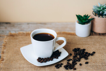 Coffee in white cup and coffee beans on sackcloth napkin. Selective focus