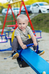 Fototapeta na wymiar Cute kid having fun on seesaw at playground. Concept of kindergarten. Vertical