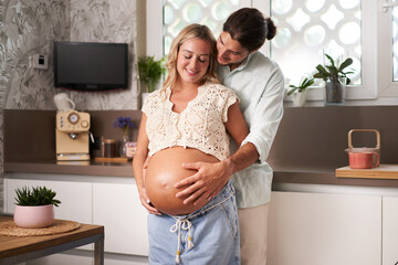 Loving caucasian couple at home in kitchen feeling baby kick together. Pregnant mom and Smiling dad...