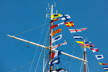 International maritime signal flags on a flagpole and masts on a sailing ship with a blue sky in the background.