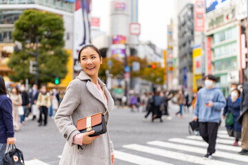 Happy Asian woman shopping and crossing street crosswalk with crowd of people at Shibuya, Tokyo,...