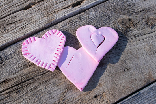 Valentine's Da themed studio shot of three pink colored clay heart shapes, the universal symbol of love and romance, on a weathered old barn wood background with copy space.