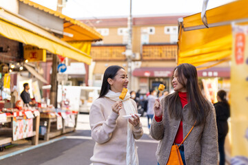 Asian woman friends eating street food sweet egg roll together while travel at fish market in Tokyo city, Japan. Attractive girl enjoy and fun outdoor lifestyle travel street market on autumn vacation