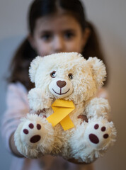 The girl holds in her hands a toy teddy bear with a yellow ribbon.