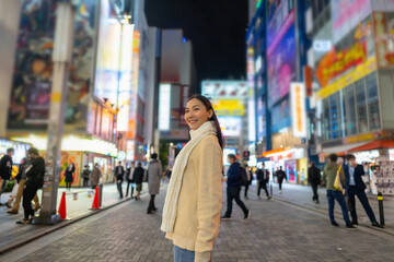 Asian woman shopping and crossing street crosswalk with crowd of people at Shibuya, Tokyo, Japan at night. Attractive girl enjoy and fun outdoor lifestyle travel in city on autumn holiday vacation.