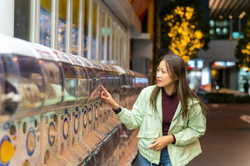 Happy Asian woman handle a doll from gashapon capsule toy vending machine while shopping at Tokyo city, Japan. Attractive girl enjoy and fun outdoor travel city street on autumn holiday vacation.