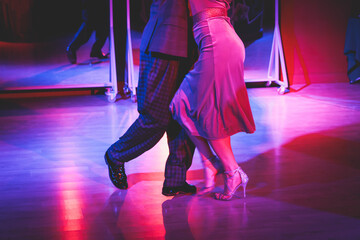 Fototapeta premium Couples dancing traditional latin argentinian dance milonga in the ballroom on a festival, tango studio, salsa, bachata and kizomba lesson in the red and purple lights, rehearsal in the dance class